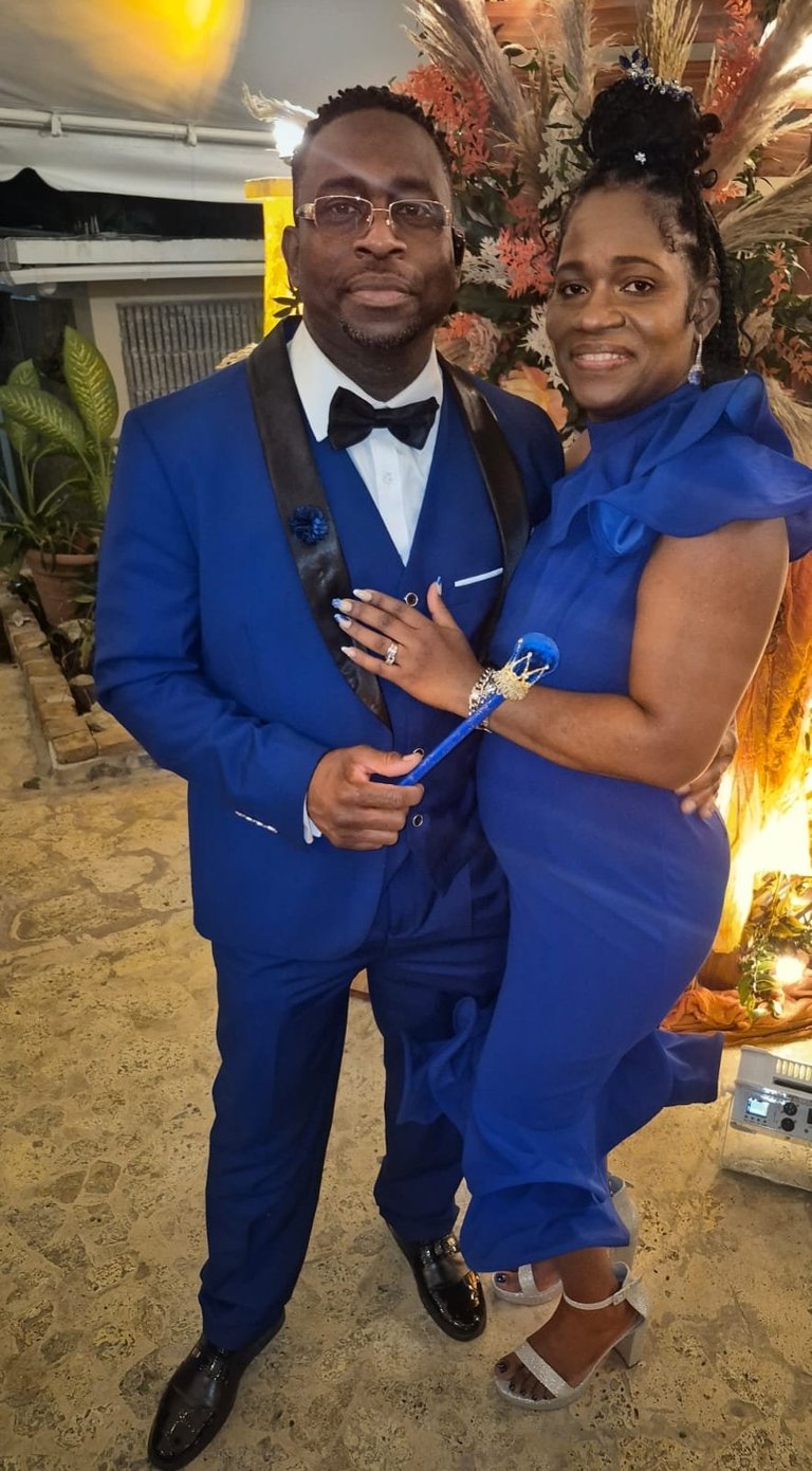 Couple in formal blue attire holding an award at an elegant event with decorative floral backdrop