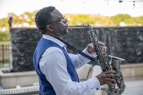 Man in blue vest playing saxophone outdoors, Minister Julian Turton