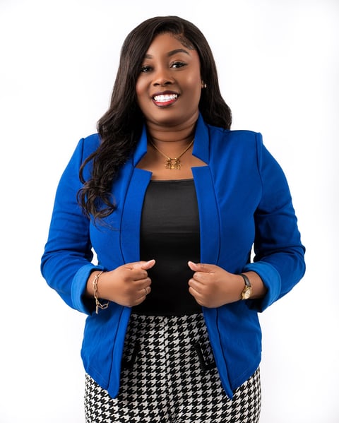 Professional headshot of a smiling woman wearing a blue blazer over a black top and houndstooth skirt against a white background