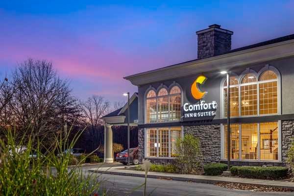 Comfort Inn hotel exterior at twilight with illuminated windows and signage, stone and siding facade, driveway visible, trees in background